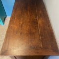 Le Bureau vintage 1960, avec un couvercle rectangulaire et une légère usure, repose sur un sol en bois contre le mur, ajoutant un charme vintage subtil à l'espace. Brocante 93