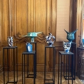 Cinq vases colorés en céramique de EVENEMENT.... sont présentés sur de grands supports noirs devant des portes en bois ornées, créant un arrangement accrocheur parfait pour toute occasion. Brocante 93