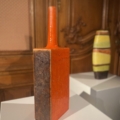 Un grand vase rectangulaire en céramique orange au col étroit, l'EVENEMENT, est exposé dans la galerie, ajoutant un sentiment d'occasion. Brocante 93