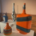 Quatre vases en céramique EVENEMENT, aux motifs orange, bleu et rayés, présentés sur des piédestaux blancs - des accents modernes idéaux pour n'importe quel espace. Brocante 93