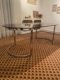La Table verre & chrome 1970, avec son plateau ovale en verre noir et ses pieds chromés, se pose sur un tapis à motifs dans un salon à la décoration chaleureuse, créant un style rétro chic. Brocante 93