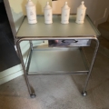 La Desserte médicale vintage 1970 est un chariot en métal des années 1970 avec un plateau en verre, présentant quatre boîtes à couvercle blanc disposées en rangée. Brocante 93