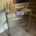 La Desserte médicale millésimée 1970, devenue un chic chariot de bar en métal avec des bouteilles et des plats en verre, se trouve élégamment près de l'escalier, sous une peinture audacieuse. Brocante 93