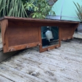 La Porte-manteaux bois 1940, une étagère murale vintage en bois avec des chevilles et un miroir central, est exposée à l'extérieur sur une terrasse en bois entourée de plantes. Brocante 93