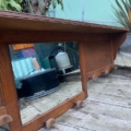 Un miroir Porte-manteaux bois 1940 avec patères est posé sur une terrasse en bois à l'extérieur, reflétant les objets et les plantes du jardin. Brocante 93