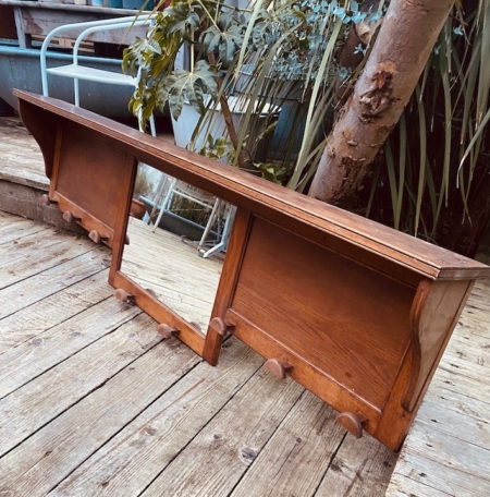 Porte-manteaux bois 1940 avec miroir central, placé à l'extérieur sur une terrasse en bois, près de plantes et d'un arbre. Brocante 93