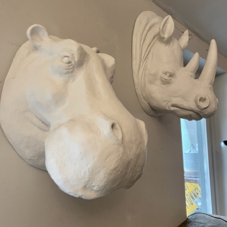 Trophées muraux résine : sculptures murales d'hippopotames et de rhinocéros, fabriquées en résine et montées côte à côte comme d'élégants trophées muraux sur un mur de couleur claire. Brocante 93