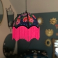 La Baladeuse bohème chic rose est un abat-jour suspendu aux motifs floraux et à la frange rose vif, parfait pour les pièces à la décoration éclectique et les miroirs. Brocante 93