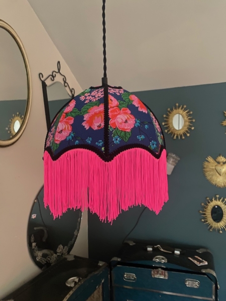 Une rose Baladeuse bohème chic avec une frange rose vif est suspendue dans une pièce aux murs sombres et aux miroirs vintage. Brocante 93