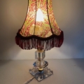 La Lampe pied en verre vintage 1940, une lampe de table avec un abat-jour en tissu à motifs et une frange rouge, est éclairée sur une surface unie. Brocante 93