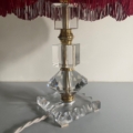 Lampe pied en verre vintage 1940 en cristal et laiton, abat-jour rouge à franges, posée sur une surface grise avec cordon blanc. Brocante 93