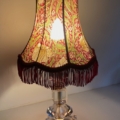 La Lampe pied en verre vintage 1940 est dotée d'un abat-jour en tissu à motifs avec des franges rouges et d'une base en verre clair à facettes, qui diffuse une lumière chaude et élégante rappelant le style classique des années 1940. Brocante 93
