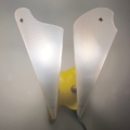 Paire d'appliques vintage 1960 : une lampe murale avec deux abat-jour givrés en forme d'ailes sur une base jaune, brillant contre un mur uni - un exemple frappant de style vintage. Brocante 93