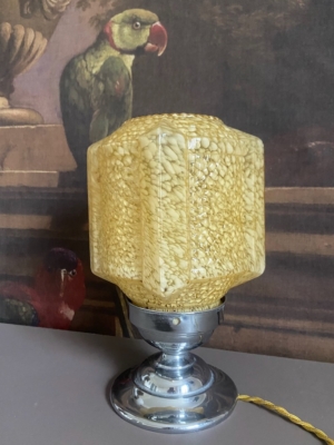 Lampe en verre 1950 avec un abat-jour en verre jaune texturé et une base chromée, placée devant un tableau de perroquets. Brocante 93