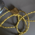 Une Lampe verre 1950 avec une prise électrique marron vintage et un cordon tressé jaune se trouve emmêlée sur une surface sombre. Brocante 93