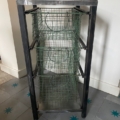 Étagère de rangement en métal avec trois paniers en grillage vert sur un sol en carrelage gris avec des motifs étoilés bleus. Brocante 93