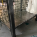 Pied de table en métal avec panier en treillis métallique sur un sol carrelé, près d'une prise murale et de carreaux en forme d'étoiles sarcelles. Brocante 93