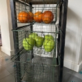 Une étagère métallique avec des paniers en fil de fer contient des oranges sur l'étagère du haut et des pommes vertes sur l'étagère du milieu. Brocante 93