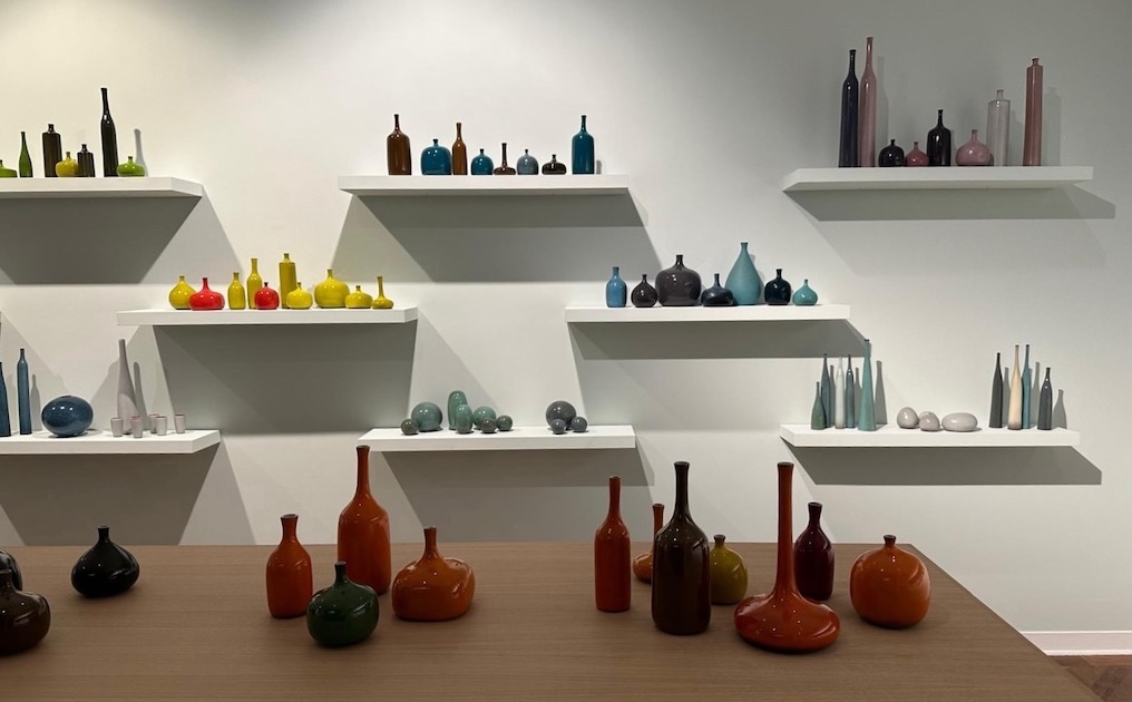 8c292460-63de-40a6-9965-0fc48b8adfb9 Des vases colorés en verre Carouche de différentes formes sont présentés sur des étagères murales blanches et une table en bois. Brocante 93