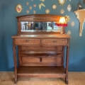 Console Art Déco 1930, une pièce en bois antique avec miroir, lampe et art mural en forme de soleil, est présentée sur un fond bleu. Brocante 93
