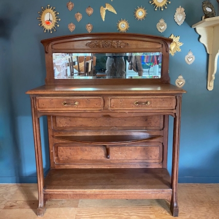 La console Art Déco 1930 est adossée à un mur bleu orné d'un soleil doré et de décorations en forme de cœur et dispose d'un miroir attenant. Brocante 93