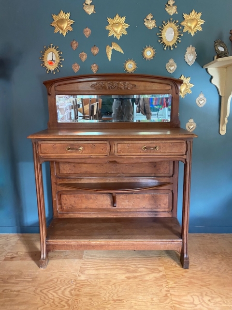 La console Art Déco 1930 est adossée à un mur bleu orné d'un soleil doré et de décorations en forme de cœur et dispose d'un miroir attenant. Brocante 93