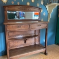 La console Art Déco 1930, un buffet antique en bois avec un miroir et deux tiroirs, est mise en valeur par l'art mural décoratif en forme de soleil en arrière-plan, ce qui témoigne d'une élégance intemporelle. Brocante 93