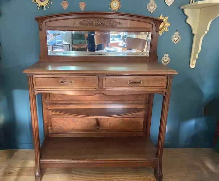 Buffet en bois avec miroir Carouche et tiroirs, placé sur un mur bleu décoré d'ornements en forme de cœur en métal. Brocante 93