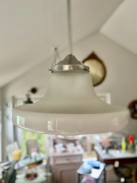 La Suspension verre & opaline 1940, un luminaire vintage en verre blanc opalin, est élégamment suspendu au plafond dans une pièce doucement éclairée. Brocante 93