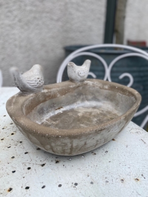 Un Bain oiseaux pierre 1960, comprenant deux figurines d'oiseaux, repose sur une table en métal blanc à l'extérieur. Brocante 93