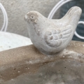 Une petite statue d'oiseau en pierre est posée sur le bord d'un Bain oiseaux pierre 1960, un bain d'oiseaux en béton vieilli. Brocante 93