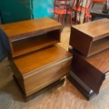 Quatre tables de nuit en bois du milieu du siècle, dont une paire de chevets SIMAT 1970, sont empilées avec des chaises rouges et une armoire verte à proximité. Brocante 93