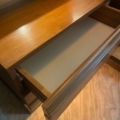 Un tiroir en bois ouvert de la Paire de chevets SIMAT 1970 révèle son intérieur vide et lumineux au-dessus d'un plancher en bois, faisant écho au style vintage classique. Brocante 93