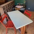 Deux chaises en métal rouge sont posées sur une Table bistrot Formica 1950 dans une pièce de style vintage à la décoration éclectique, évoquant le charme des années 1950. Brocante 93