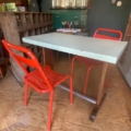 Dans une pièce confortable et éclectique avec des planchers en bois, on trouve une table bistrot Formica 1950 avec un plateau vert pâle et deux chaises en métal rouge. Brocante 93