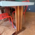 Une table bistrot Formica 1950 avec un plateau vert et deux chaises métalliques rouges est posée sur un sol en bois dans une pièce d'inspiration vintage. Brocante 93