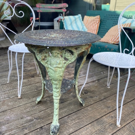 Guéridon de jardin en fonte 1940, table ronde en métal ornée, accompagnée de deux chaises métalliques blanches sur terrasse en bois. Brocante 93