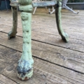 Gros plan d'un pied altéré du Guéridon de jardin en fonte 1940, en forme de patte d'animal et fabriqué en fonte, reposant sur une terrasse en bois. Brocante 93