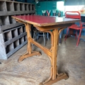 La Table de bistrot Formica rouge 1950, avec son plateau rouge vif, est posée sur un plancher en bois dans une pièce au décor éclectique. Brocante 93