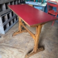 La Table de bistrot Formica rouge 1950, un bureau vintage en bois avec un plateau en Formica rouge, est posée sur un sol en bois au milieu de meubles éclectiques. Brocante 93
