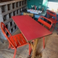 Une scène de café inspirée des années 1950 comprend une table de bistrot Formica rouge 1950 et deux chaises métalliques rouges assorties, le tout posé sur un sol en bois classique. Brocante 93