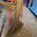 Gros plan d'un pied de table en bois sur un plancher en bois, avec des chaises de bistrot Formica rouge 1950 en arrière-plan, mettant en valeur le charme vintage de la Table de bistrot Formica rouge 1950. Brocante 93