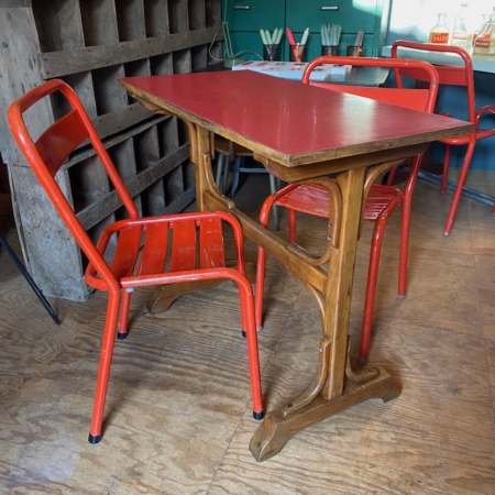 Un café confortable présente la Table de bistrot Formica rouge 1950 associée à des chaises en métal rouge, entourée d'un décor en bois chaleureux et en métal industriel. Brocante 93