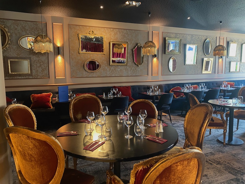 Intérieur élégant d'un restaurant avec des chaises Carouche d'époque, des tables dressées, des miroirs au mur et un éclairage chaleureux. Brocante 93