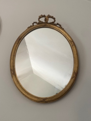 Le Miroir à entrelacs, doté d'un cadre rond et doré et d'un plateau orné, s'accroche élégamment à un mur blanc uni. Brocante 93