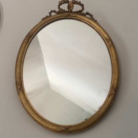 Le Miroir à entrelacs, doté d'un cadre rond et doré et d'un plateau orné, s'accroche élégamment à un mur blanc uni. Brocante 93