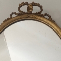 Le Miroir à entrelacs présente un cadre doré orné de motifs entrelacés et d'un nœud décoratif au sommet, présenté sur un mur blanc uni. Brocante 93