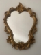 Le Miroir Rococo 1960 présente un cadre doré décoratif avec des motifs floraux et des volutes complexes. Il respire l'élégance vintage et le style rococo classique lorsqu'il est accroché gracieusement à un mur. Brocante 93