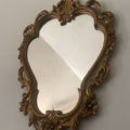 Le Miroir Rococo 1960, un miroir vintage avec un cadre doré orné de détails floraux, s'inspire du style Rococo et s'accroche à un mur uni de couleur claire. Brocante 93