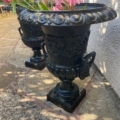 La Paire de vases Médicis XXème siècle, en noir orné et garnie de fleurs roses, illumine un patio en pierre baigné de soleil-une touche d'élégance intemporelle. Brocante 93